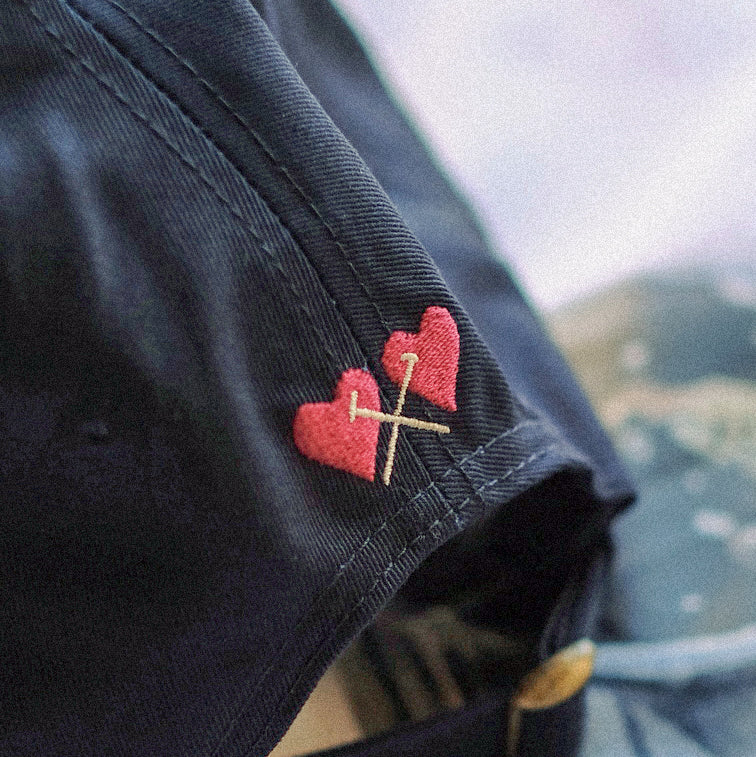 Black fabric with red heart design and gold cross, blurred natural background