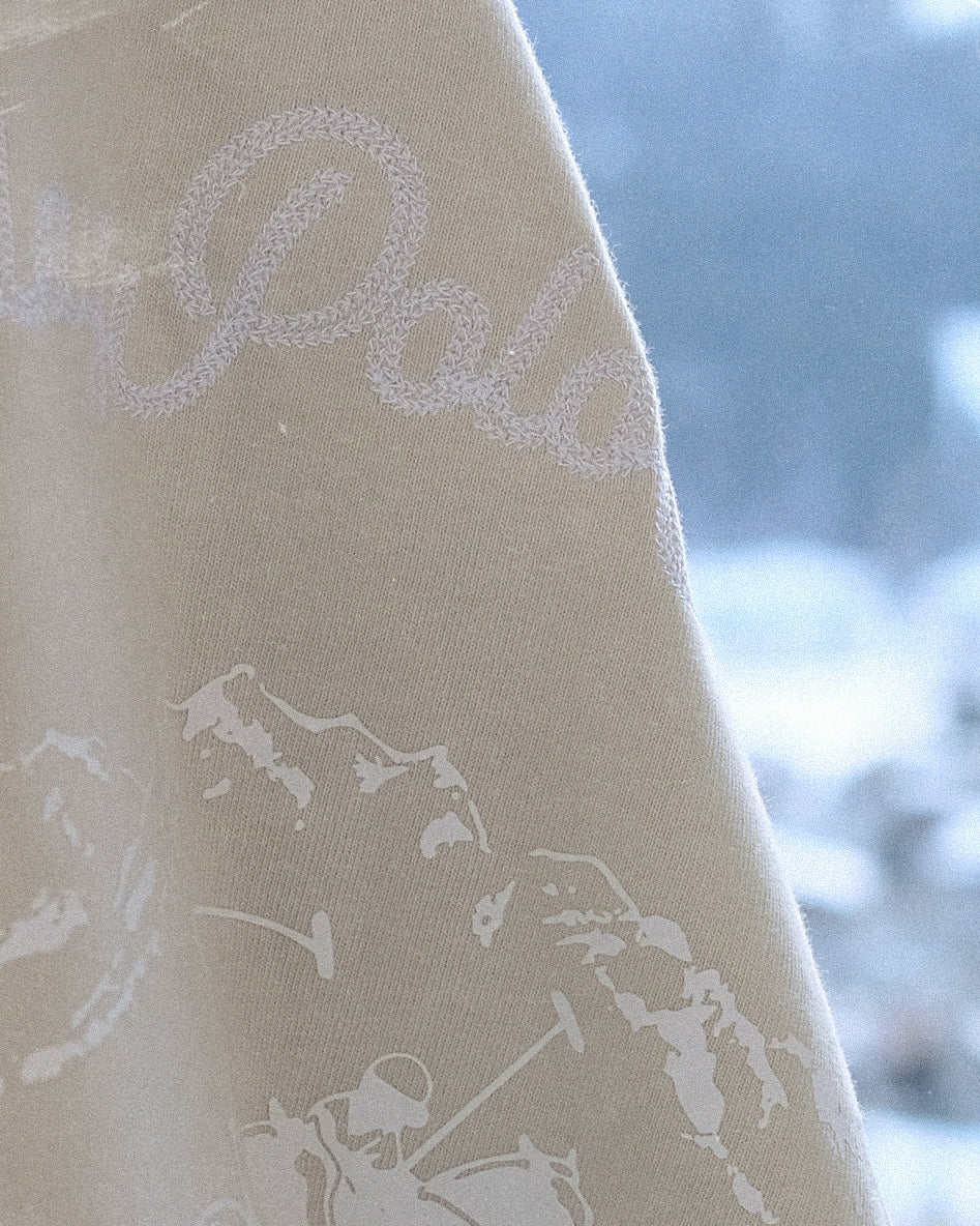 Close-up of a beige fabric with white text and mountain designs, blurred snowy background