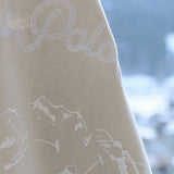 Close-up of a beige fabric with white text and mountain designs, blurred snowy background