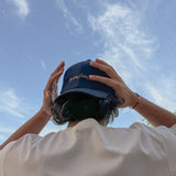 Person holding a navy blue cap with text against a clear blue sky