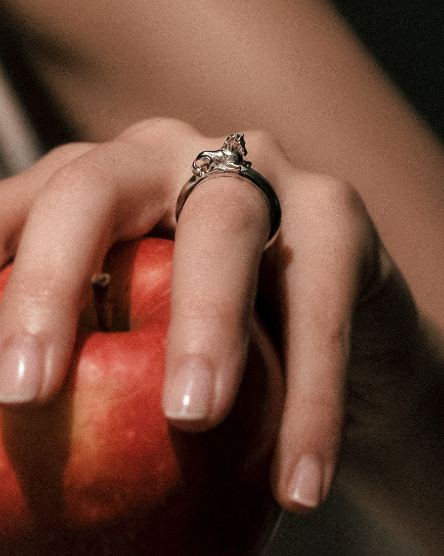Hand holding a red apple with a silver horse ring on a blurred background