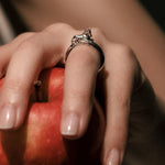 Hand holding a red apple with a silver horse ring on a blurred background